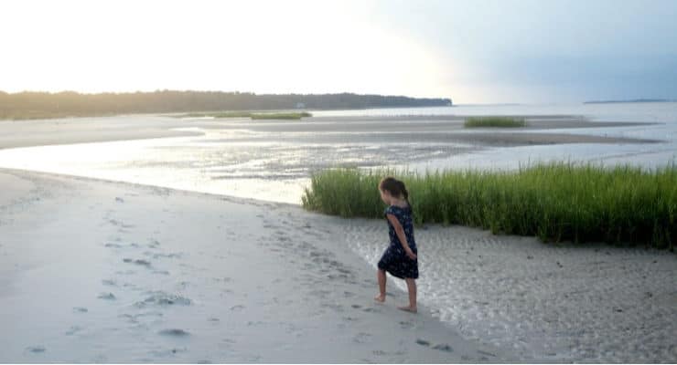 Small girl walking on a sandy beach with grasses.