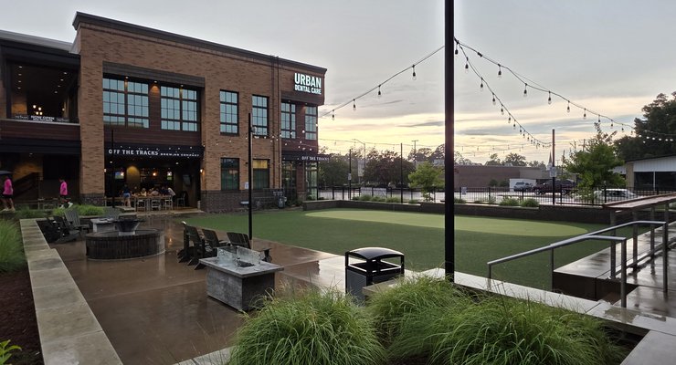 Wide view of Hobo's restaurant patio with turf play area, string lights, fire pits, and the restored brick building in Rock Hill SC